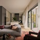 Bright and modern living space featuring a grey L-shaped sofa with cushions, a dark armchair, and large glass doors opening to a garden.