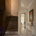 Elegant foyer with a curved staircase, marble flooring, and minimalist decor, leading to a sunlit room framed by a steel door.