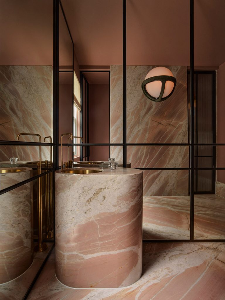Stylish bathroom featuring a round marble sink, warm pink tones, sleek black framing, and a modern spherical light fixture.