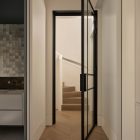 A black steel-framed glass door opens into a light hallway with a herringbone wooden floor, leading to a staircase beyond.