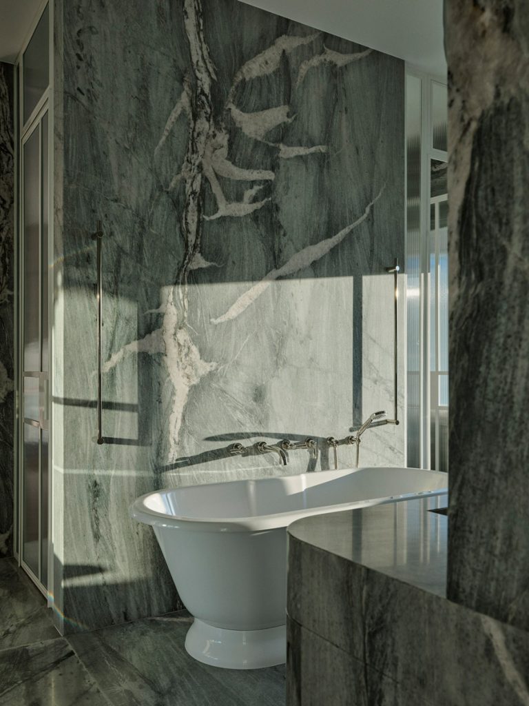 Elegantly designed bathroom featuring a freestanding white bathtub against a backdrop of striking green marble with natural veining.