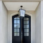 Black wrought iron entry doors with large glass panels, framed by a light stone façade and a hanging lantern above.