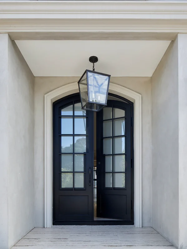 Black wrought iron entry doors with large glass panels, framed by a light stone façade and a hanging lantern above.